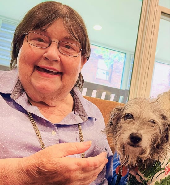 A woman smiles with a small therapy dog in her lap